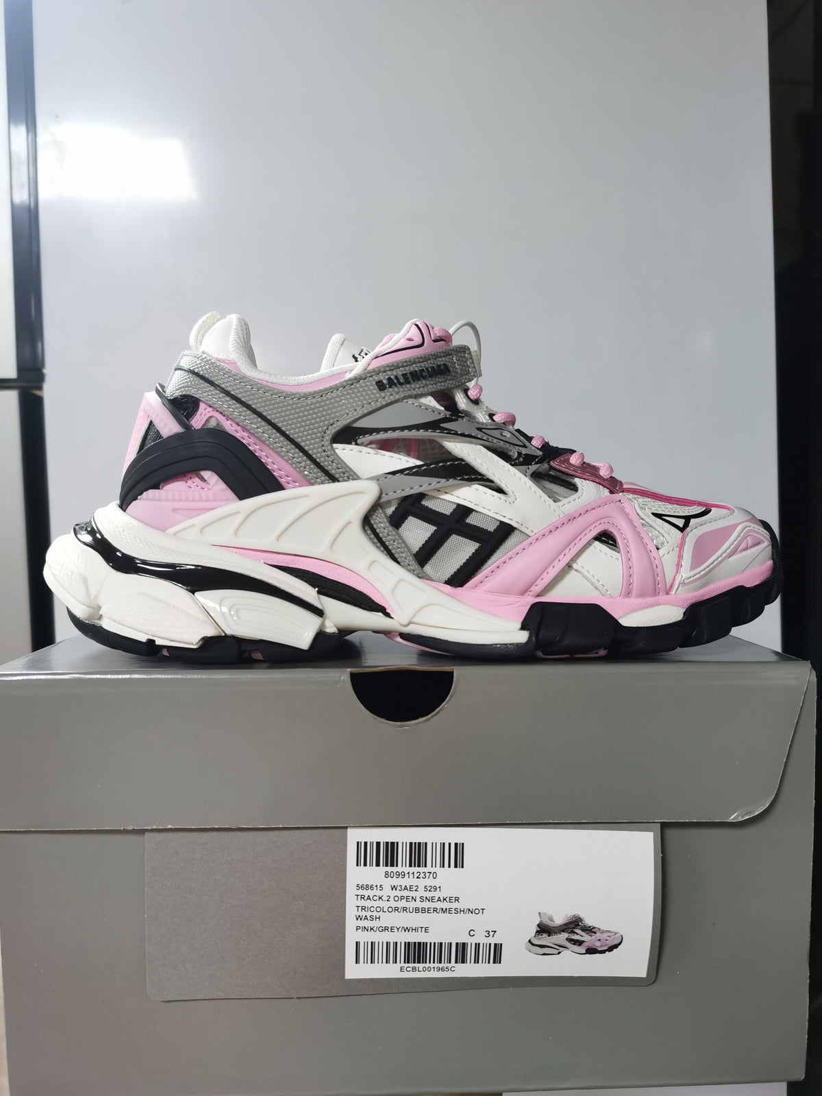 Side profile of the Balenciaga Track.2 sneaker on its box, with the pink, grey and white colorway and product label visible.