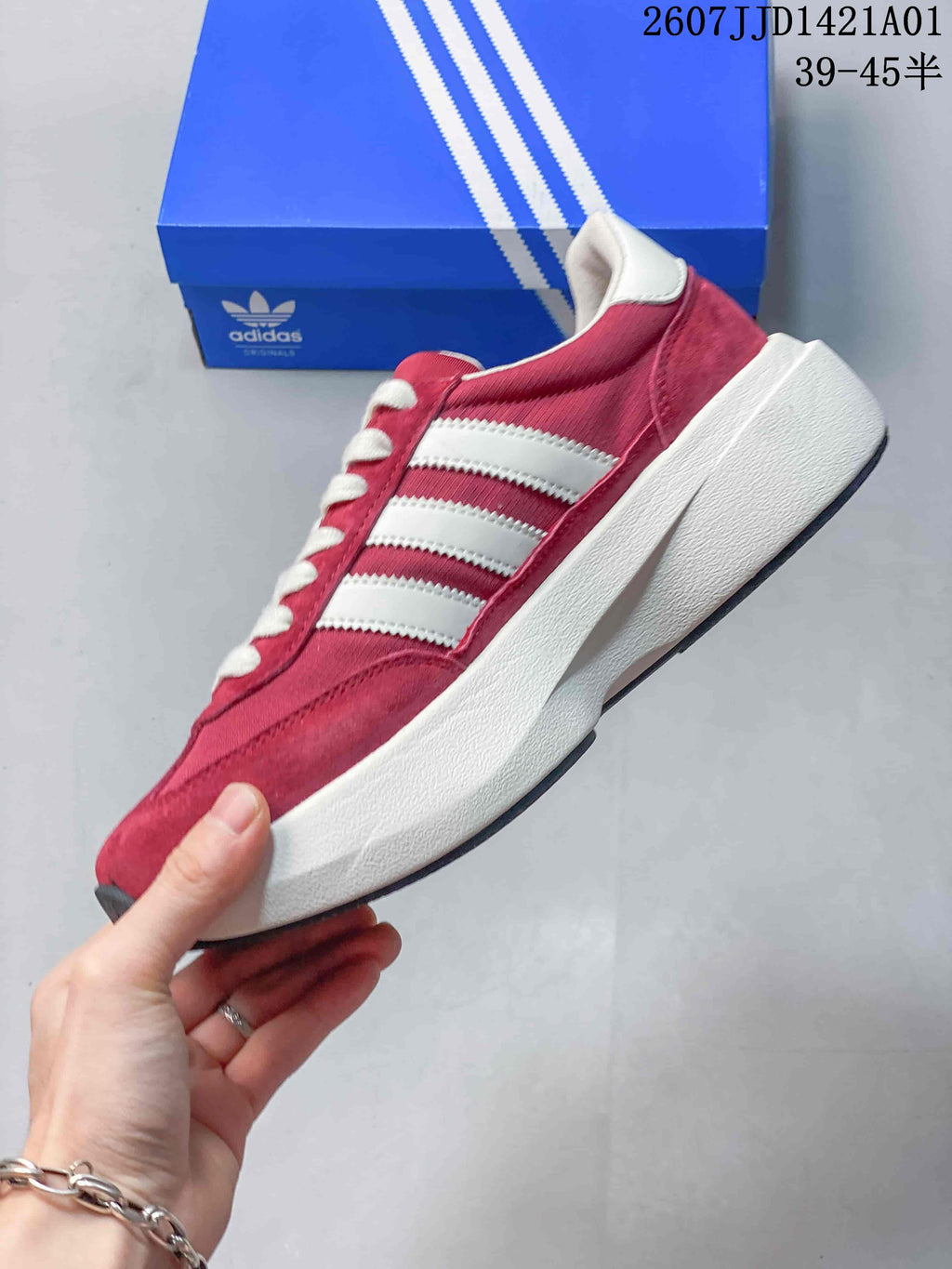 Red Adidas Adizero SL 72 Pro sneaker with white stripes and thick white sole, shown in profile beside a blue shoe box.