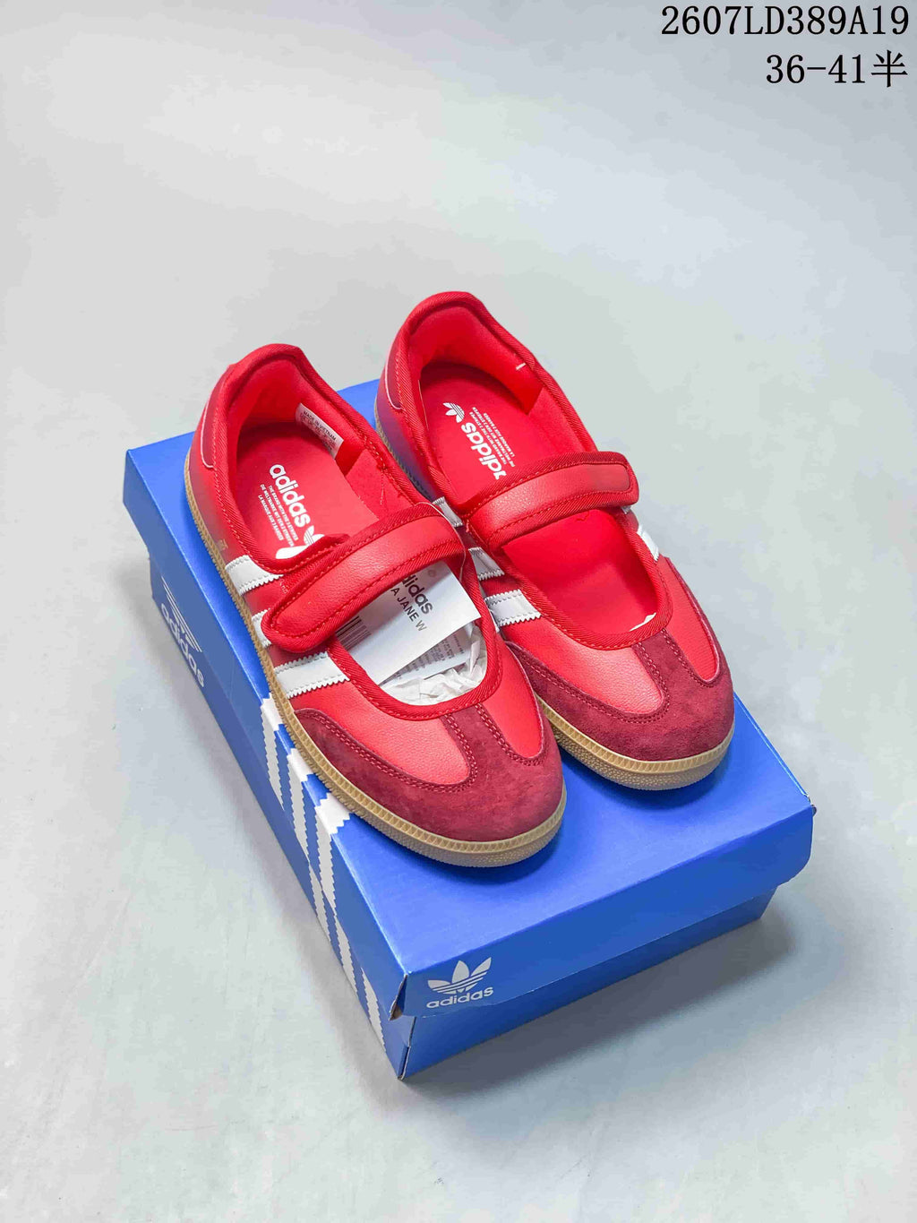 Red and white adidas Samba Jane sneakers displayed on a blue adidas shoe box, with a visible hook-and-loop strap and gum-colored outsole.