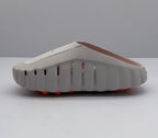 Rear-side view showing the scalloped sole edge, side ventilation openings, and orange outsole elements of the slide sandal.