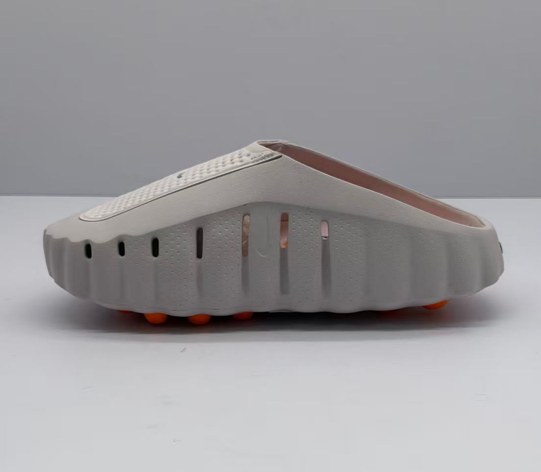 Rear-side view showing the scalloped sole edge, side ventilation openings, and orange outsole elements of the slide sandal.