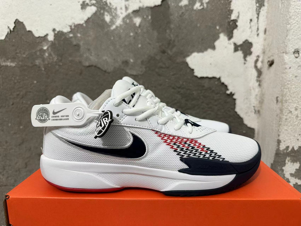 Side view of a white Nike basketball shoe with a black swoosh, red-and-black patterned panel, and dark toe accent.