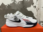 Side view of a white Nike basketball shoe with a black swoosh, red-and-black patterned panel, and dark toe accent.