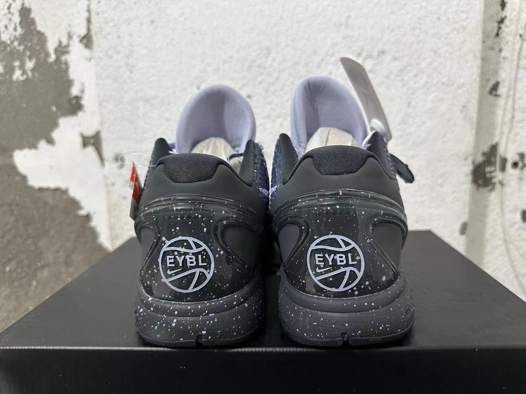 Rear view of purple and black Nike Kobe basketball shoes with speckled soles and EYBL graphics.