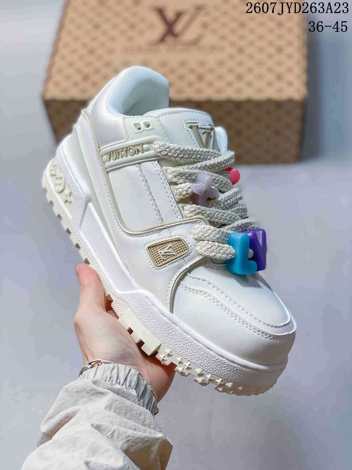 Angled side view of a white Louis Vuitton sneaker showing the layered upper, braided laces, decorative charms and textured outsole; image text shows code 2607JYD263A23 and size range 36–45.