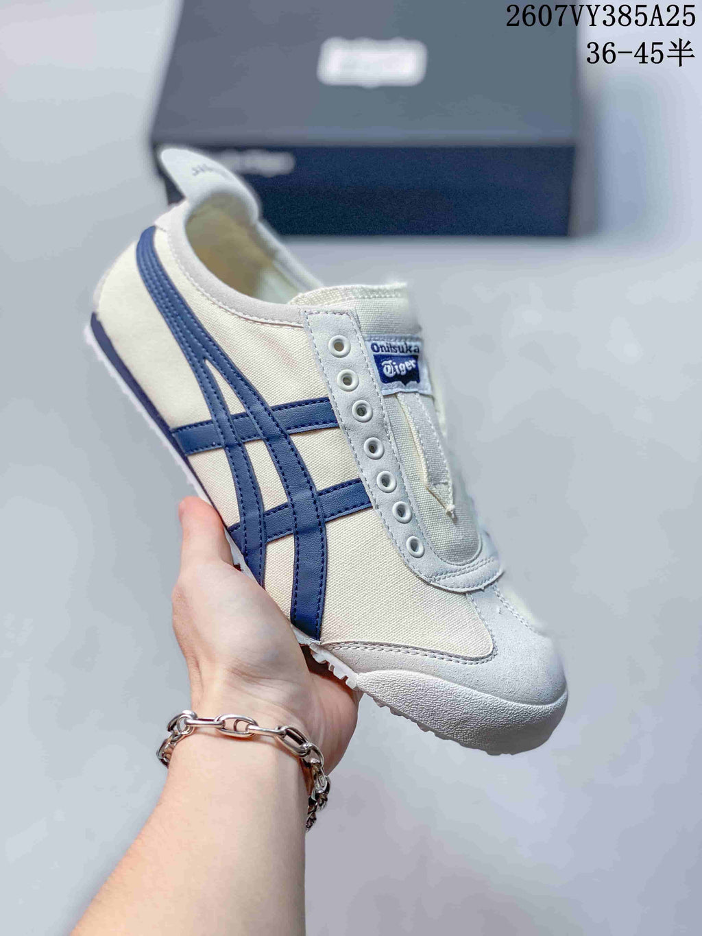 Cream slip-on sneaker with dark blue side stripes and a white outsole, shown beside a branded shoe box.