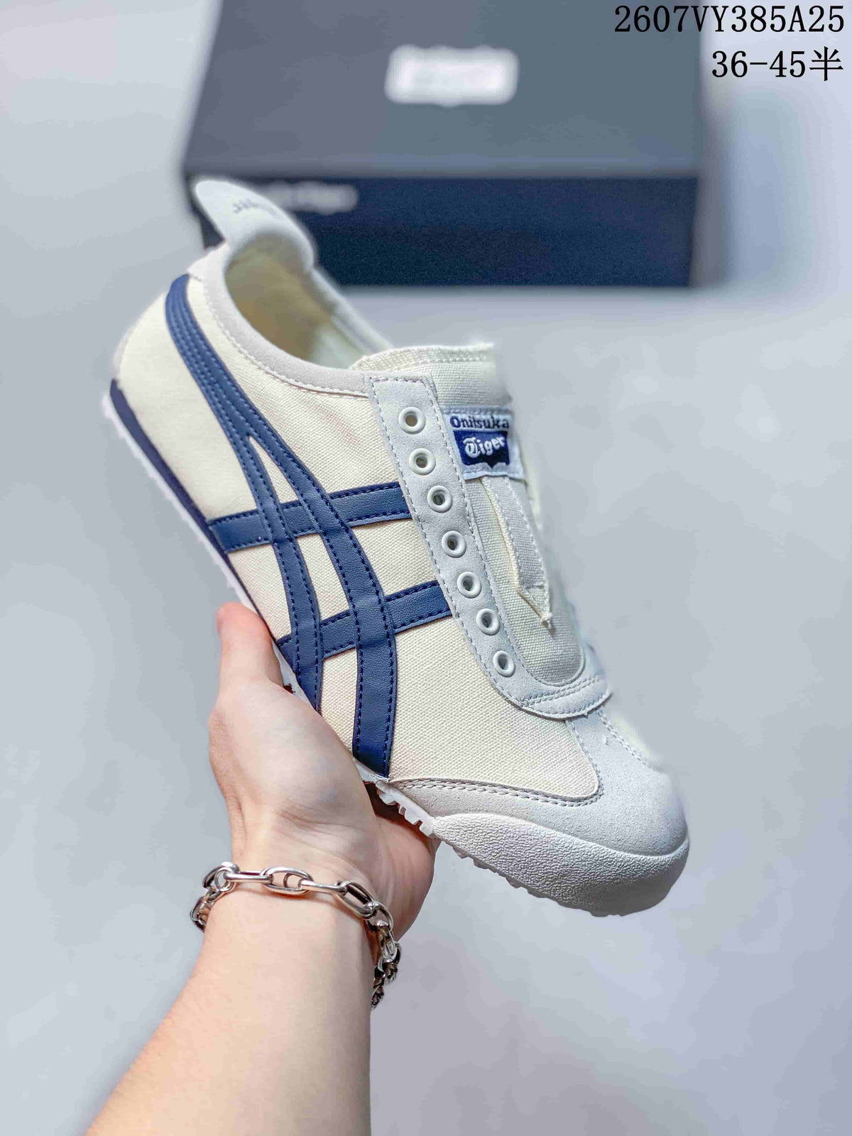 Cream slip-on sneaker with dark blue side stripes and a white outsole, shown beside a branded shoe box.