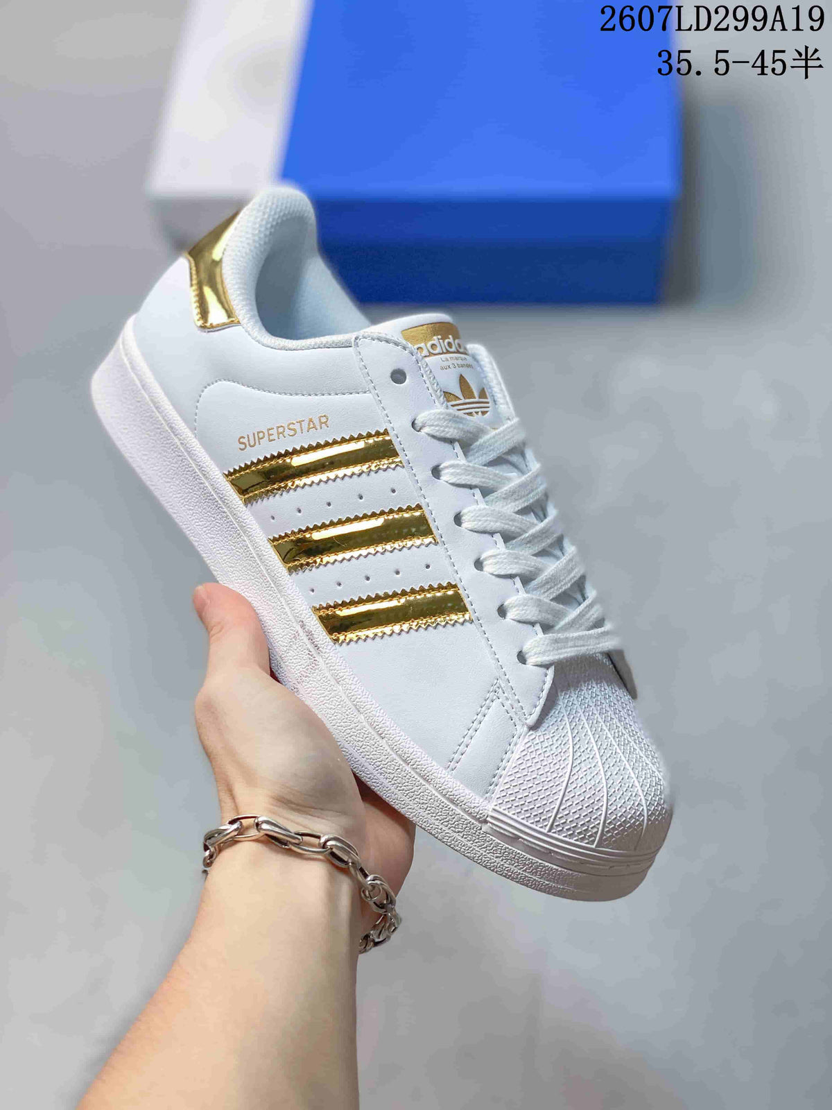 White adidas Superstar sneaker with metallic gold serrated stripes and gold heel accent.