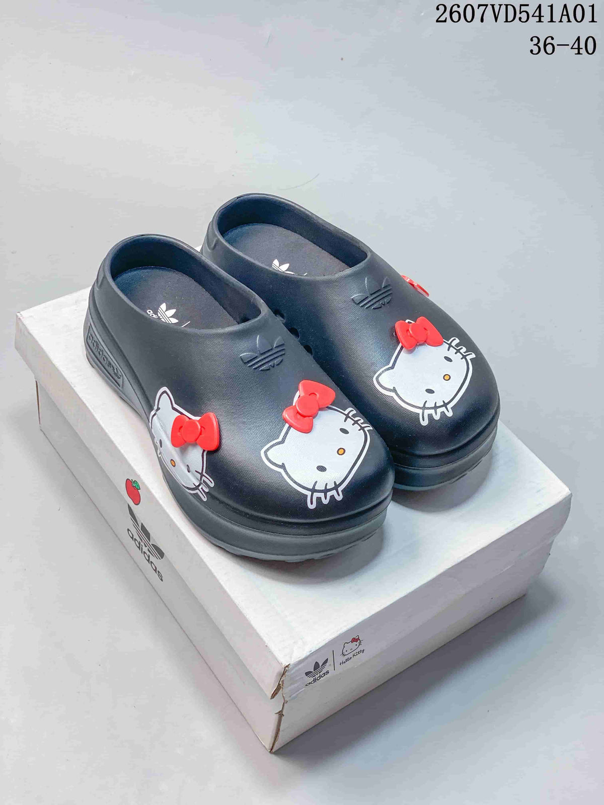 Pair of charcoal clog mules with Hello Kitty graphics and red bow details, shown on a box.