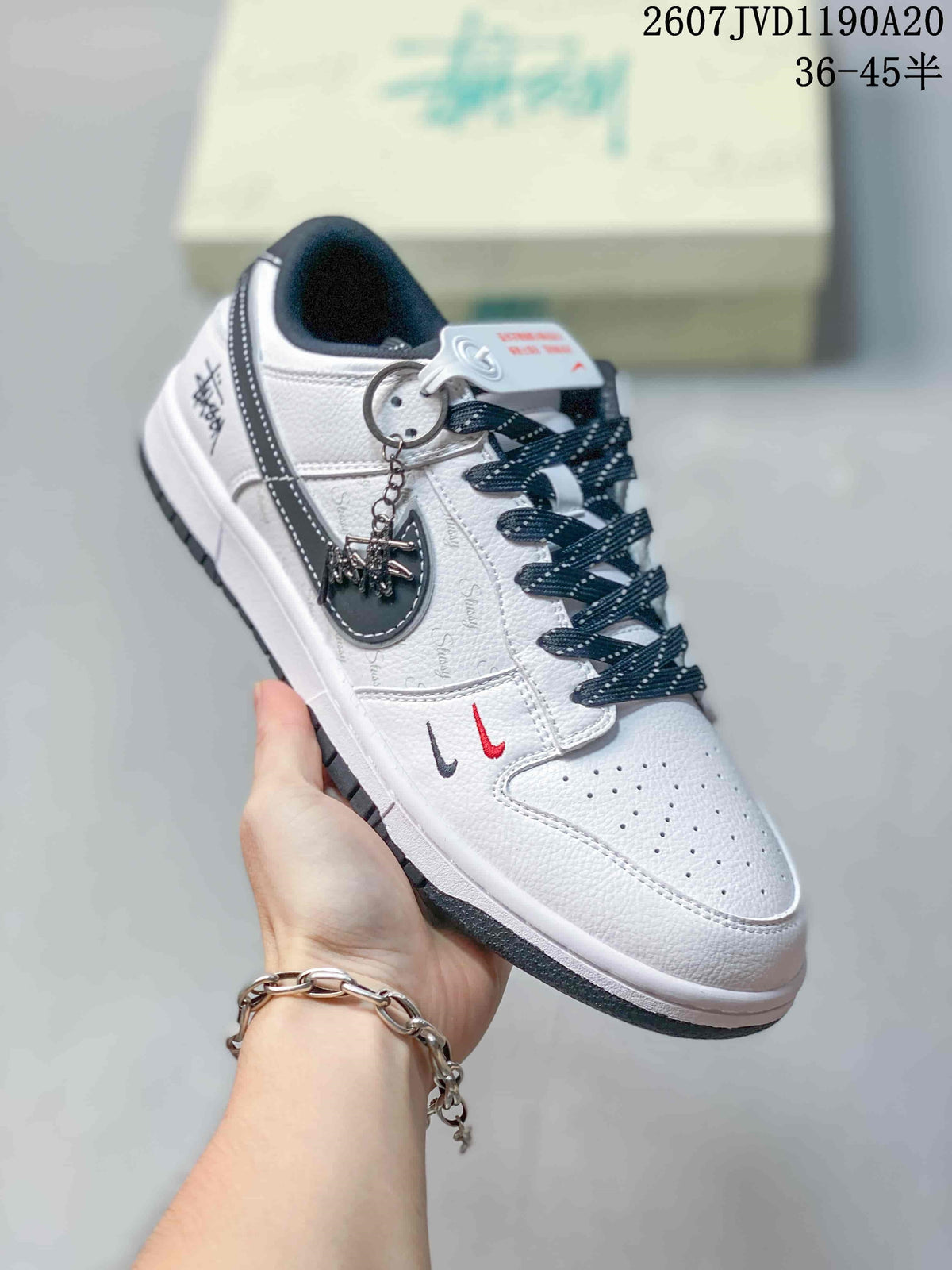 Close-up of an off-white Nike SB Dunk Low sneaker with black laces, contrasting Swoosh, attached accessory and dark outsole.