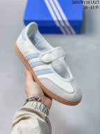 Close-up of a white Samba Jane sneaker with light blue stripes, a hook-and-loop strap and gum-style outsole.