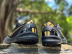 Rear view of the sneaker pair showing black heel panels, gold striping, and heel graphics.