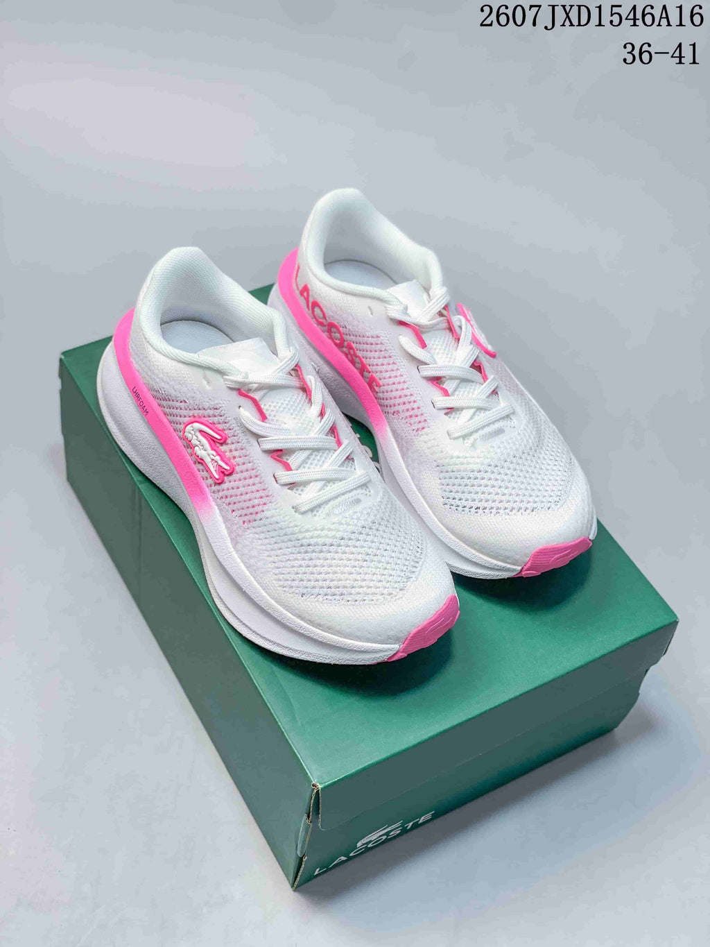 Pair of white and pink Lacoste Neo Run sneakers displayed on a green shoe box.