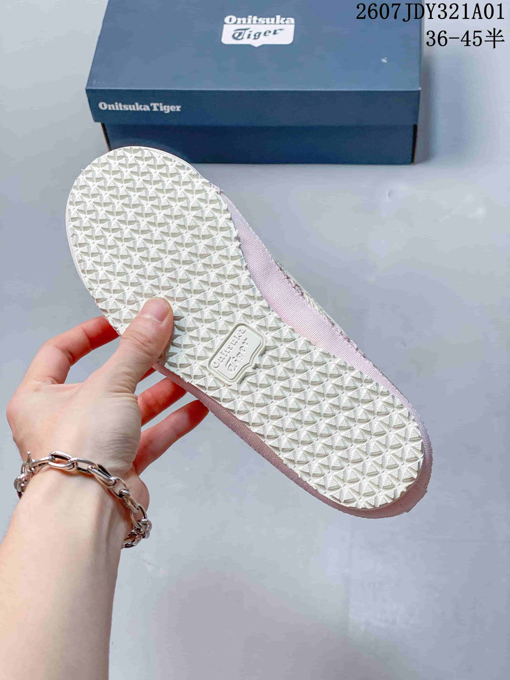 Textured light-colored outsole of a pink slip-on shoe, with a branded shoebox in the background.