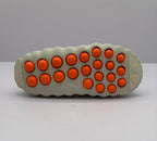 Underside view showing rows of orange circular outsole elements and a textured beige perimeter.
