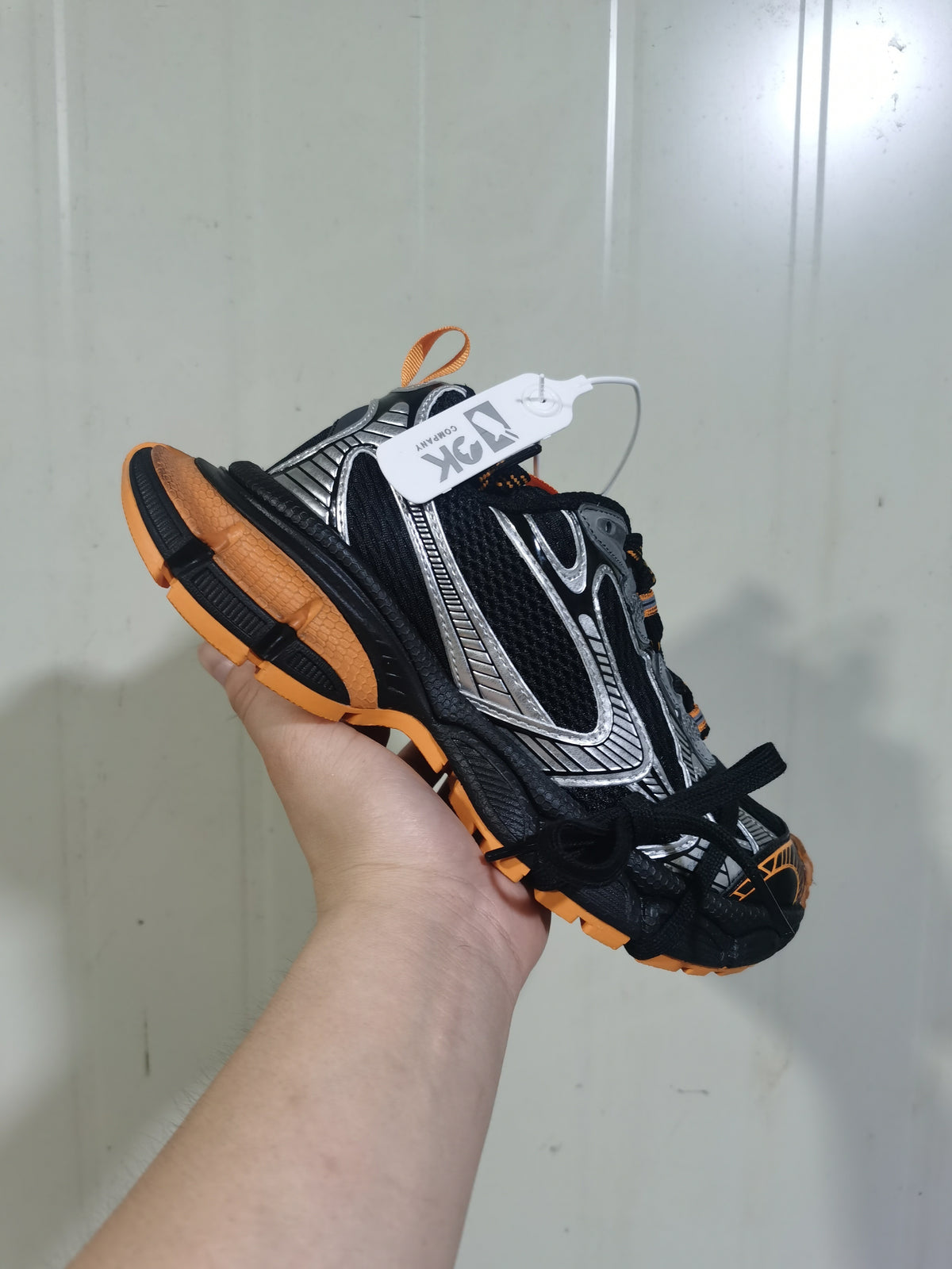 Angled view of the black sneaker showing silver side detailing, orange outsole sections, and black laces.
