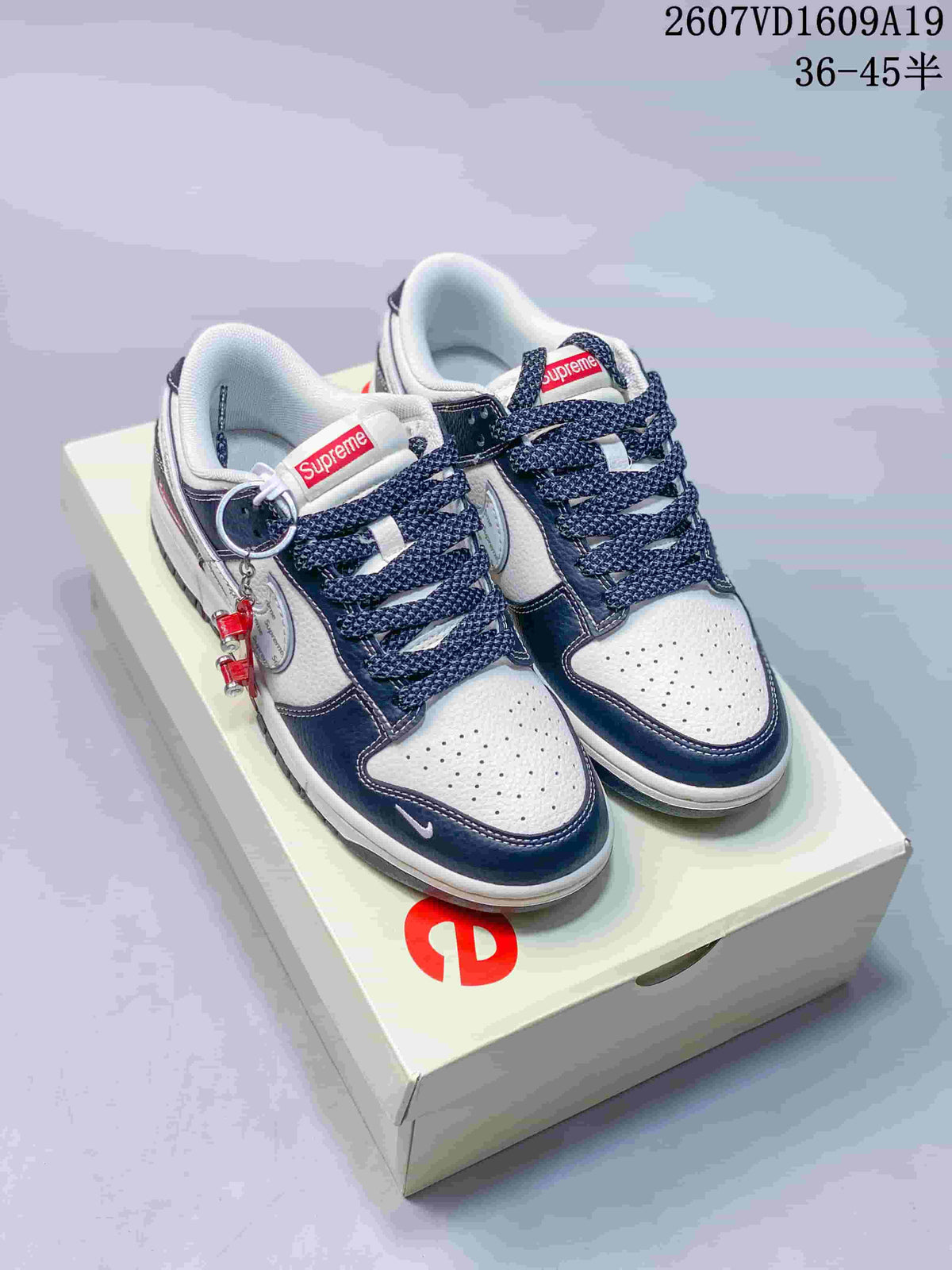 Pair of Nike Dunk Low sneakers featuring white uppers, dark navy overlays, patterned laces and red accent details.