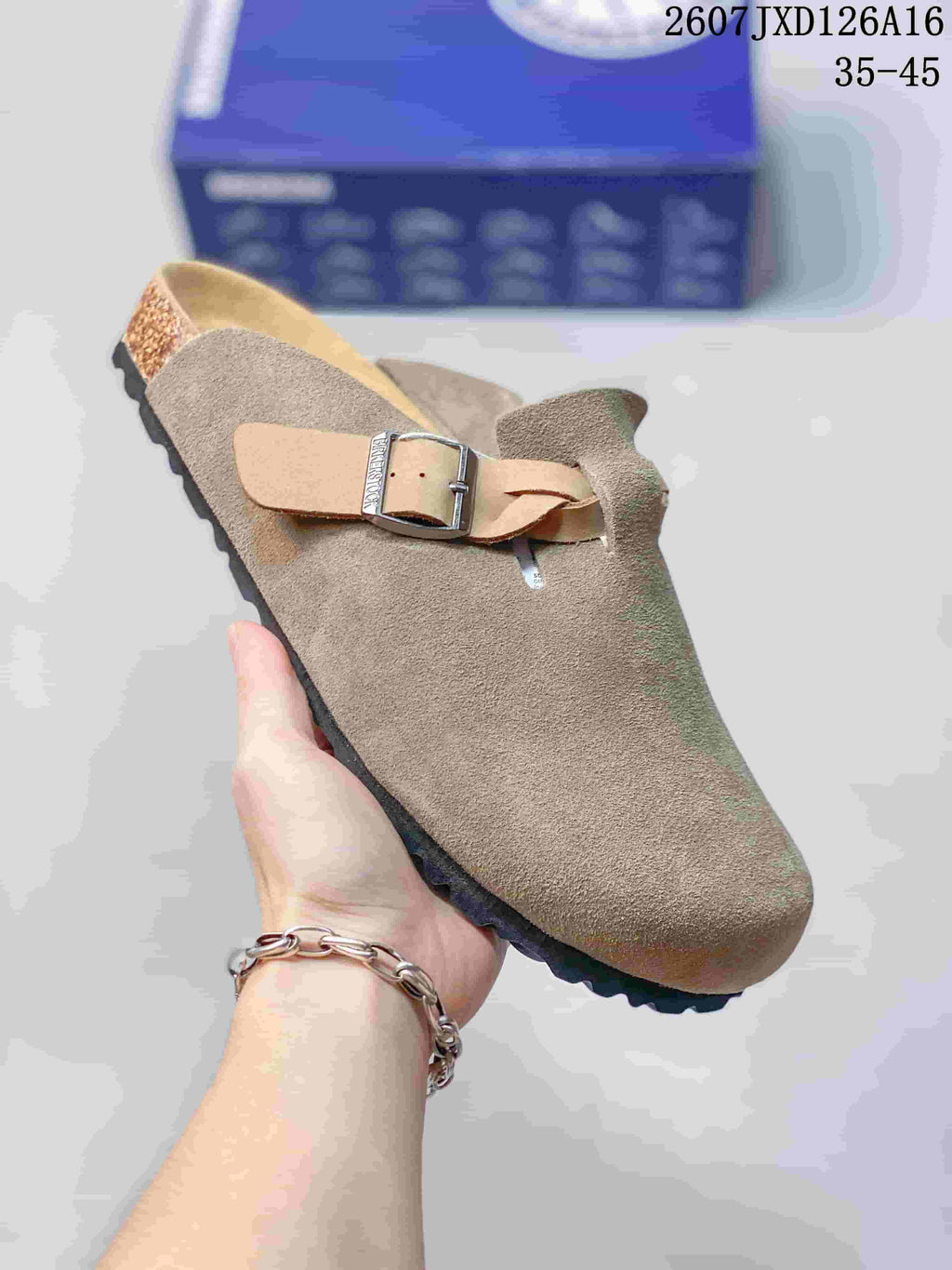 Angled side view highlighting the taupe upper, tan buckle strap and black outsole of the closed-toe mule.