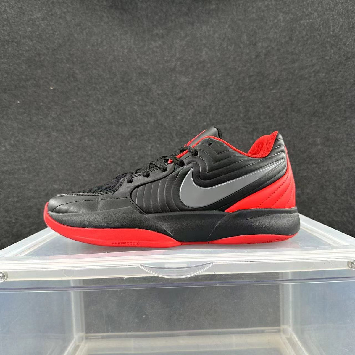 Black and red low-top Nike sneaker with a contrasting swoosh, displayed on a clear stand.