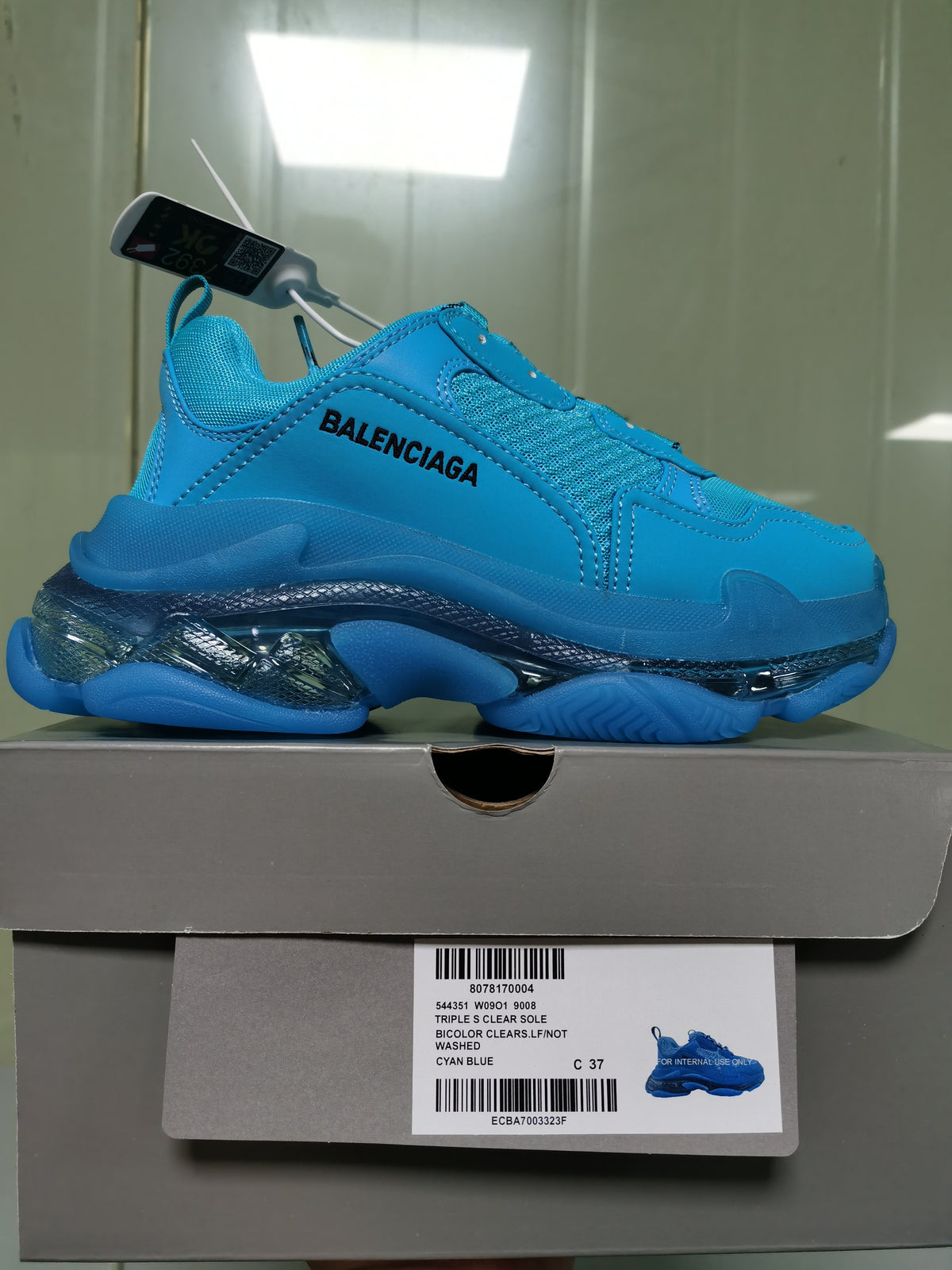Side profile of the cyan blue sneaker resting on its box, with the box label identifying Triple S Clear Sole, Cyan Blue, and size C 37.