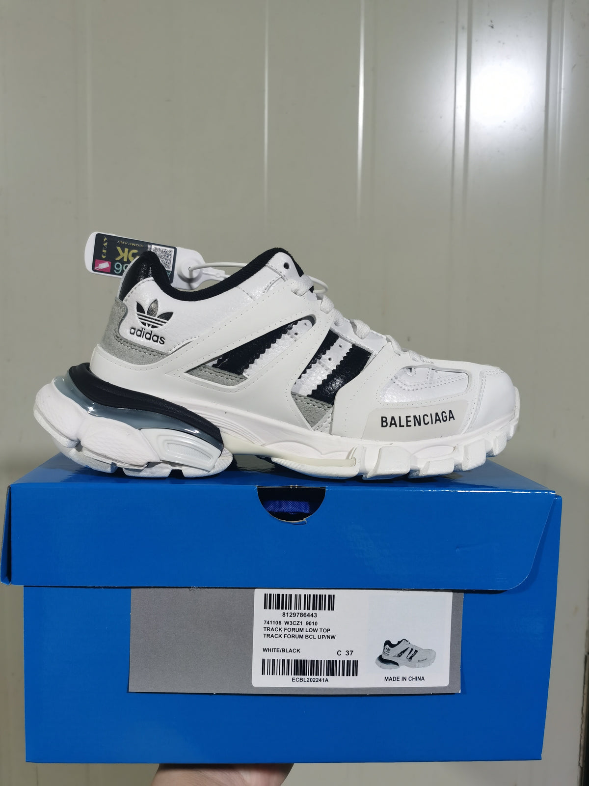 White and black Balenciaga x adidas low-top sneaker displayed on a blue shoe box; the box label shows style code 9010, color White/Black and size C 37.