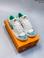 Pair of white and green Nike Blazer Low ’77 Jumbo sneakers displayed on an orange shoebox.