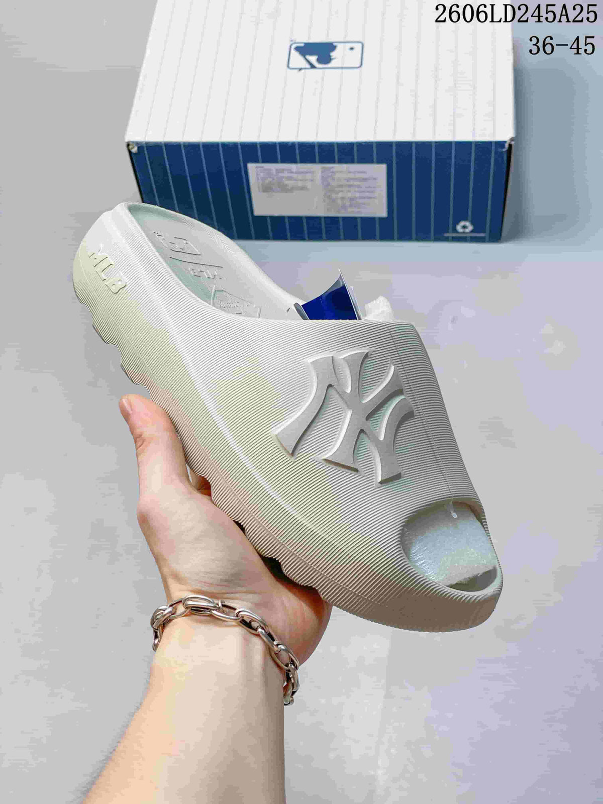 Close side view of a light-colored slide sandal with raised NY lettering.
