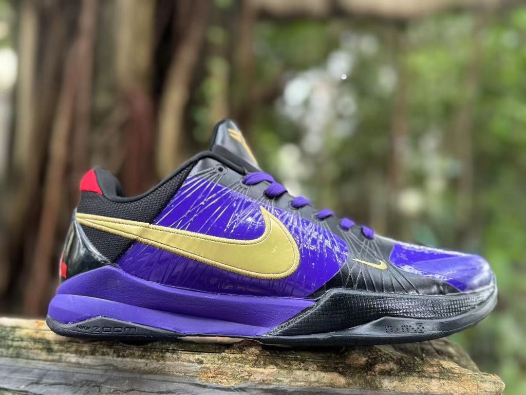 Side profile showing purple panels, black overlays and gold-colored branding on a Nike Kobe 5 shoe.