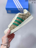 Side profile showing the beige patterned upper, green three-stripe detail, shell toe, and off-white sole.