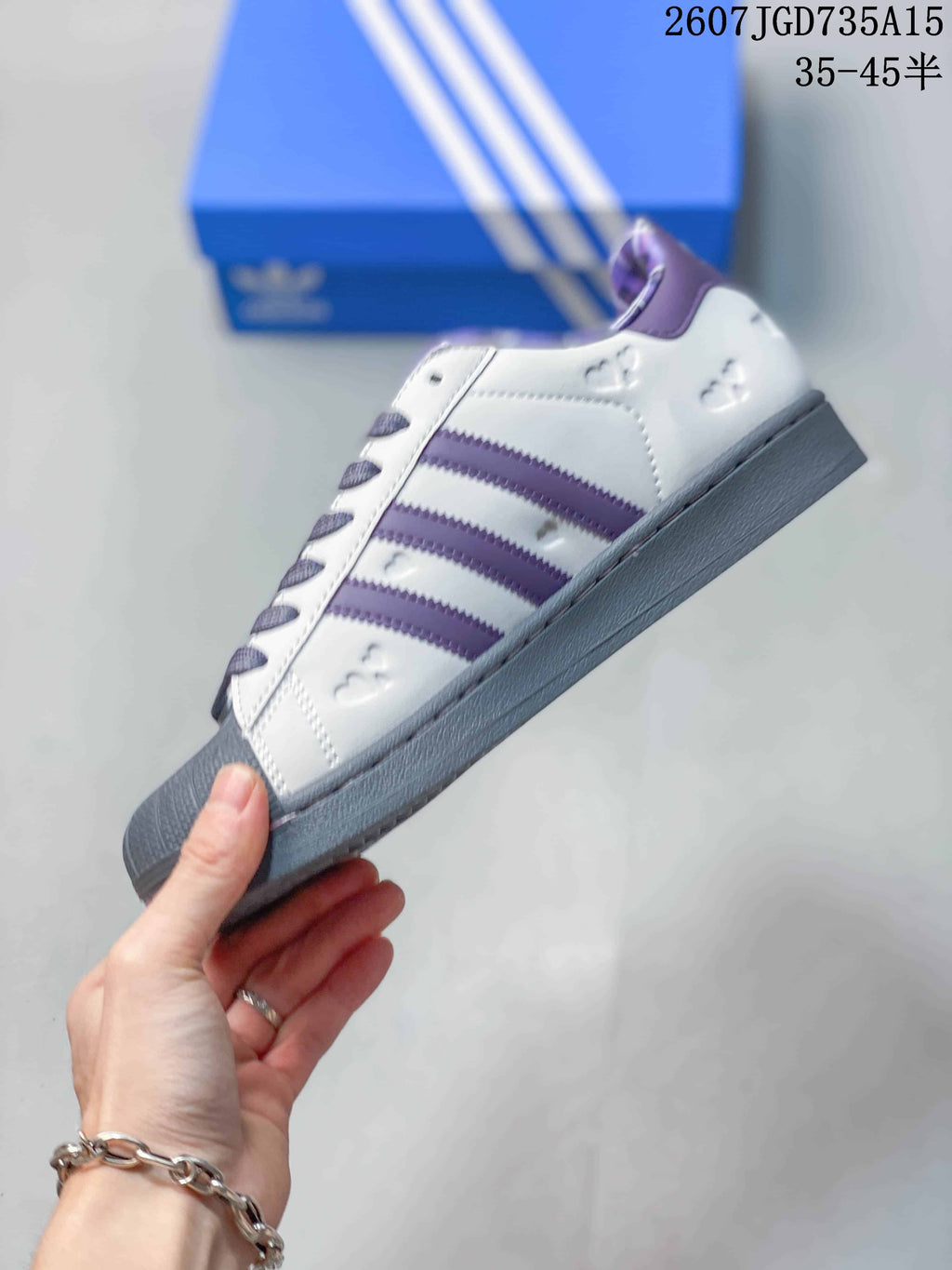 Side profile of the white sneaker with purple stripes, gray sole and decorative perforation details.