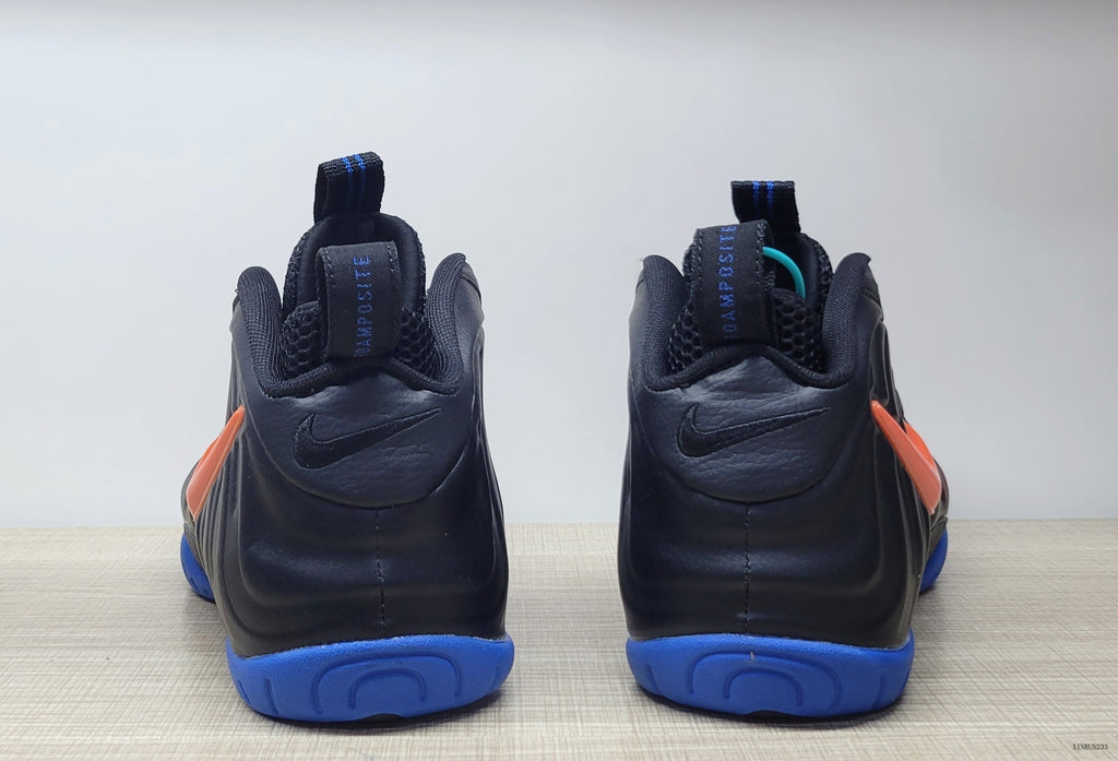 Rear view of the black Nike Air Foamposite Pro pair with blue outsole sections and orange side accents.