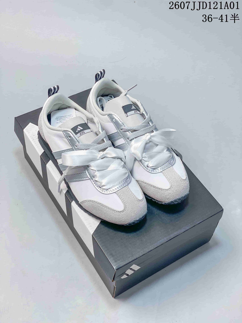 Pair of white and gray adidas JOG sneakers with ribbon laces on a shoebox