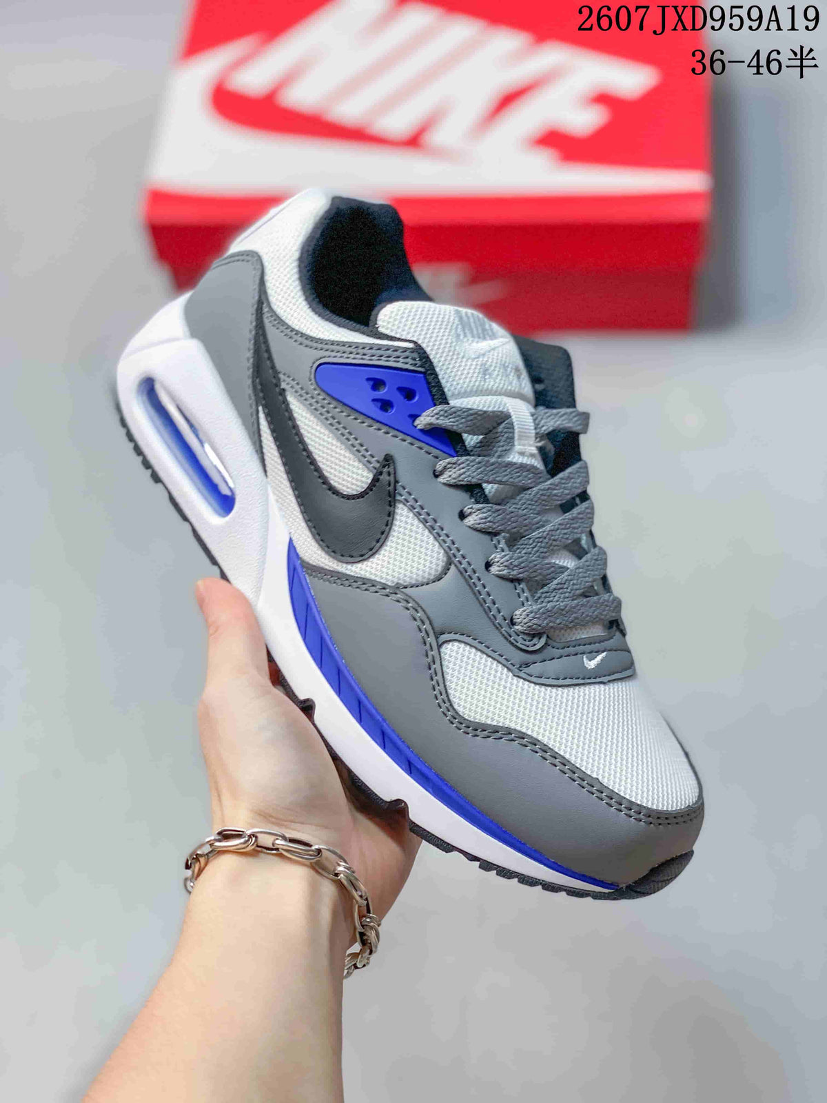 Three-quarter side view of the gray, white, and blue sneaker with lace-up construction and a visible heel cushioning unit.
