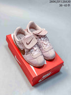 Pale pink low-top sneakers with brown Swooshes and flap details over the laces, photographed on a red shoe box.