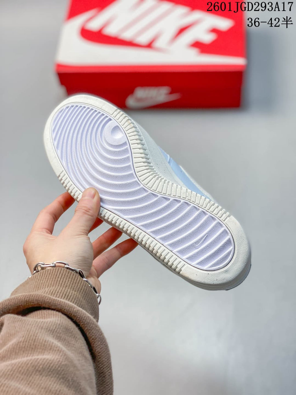 Underside view of a light-colored sneaker showing the patterned rubber outsole and textured perimeter tread.