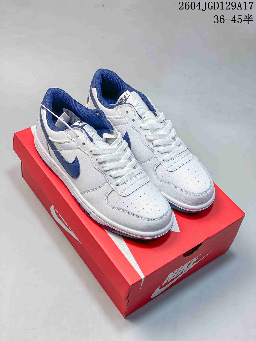 Pair of white low-top sneakers with blue Swoosh details on a red shoe box