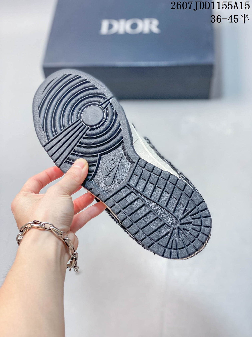 Close view of the dark textured outsole with circular forefoot tread and raised Nike branding; Dior-branded box in the background.