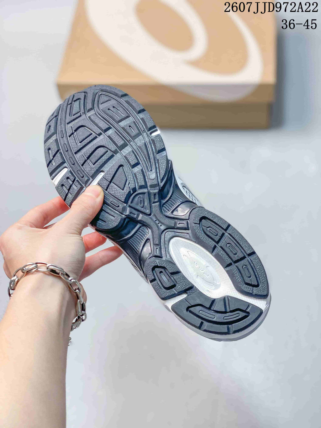 Close view of the patterned rubber outsole and tread sections of a white and silver ASICS sneaker.