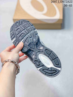 Close view of the patterned rubber outsole and tread sections of a white and silver ASICS sneaker.