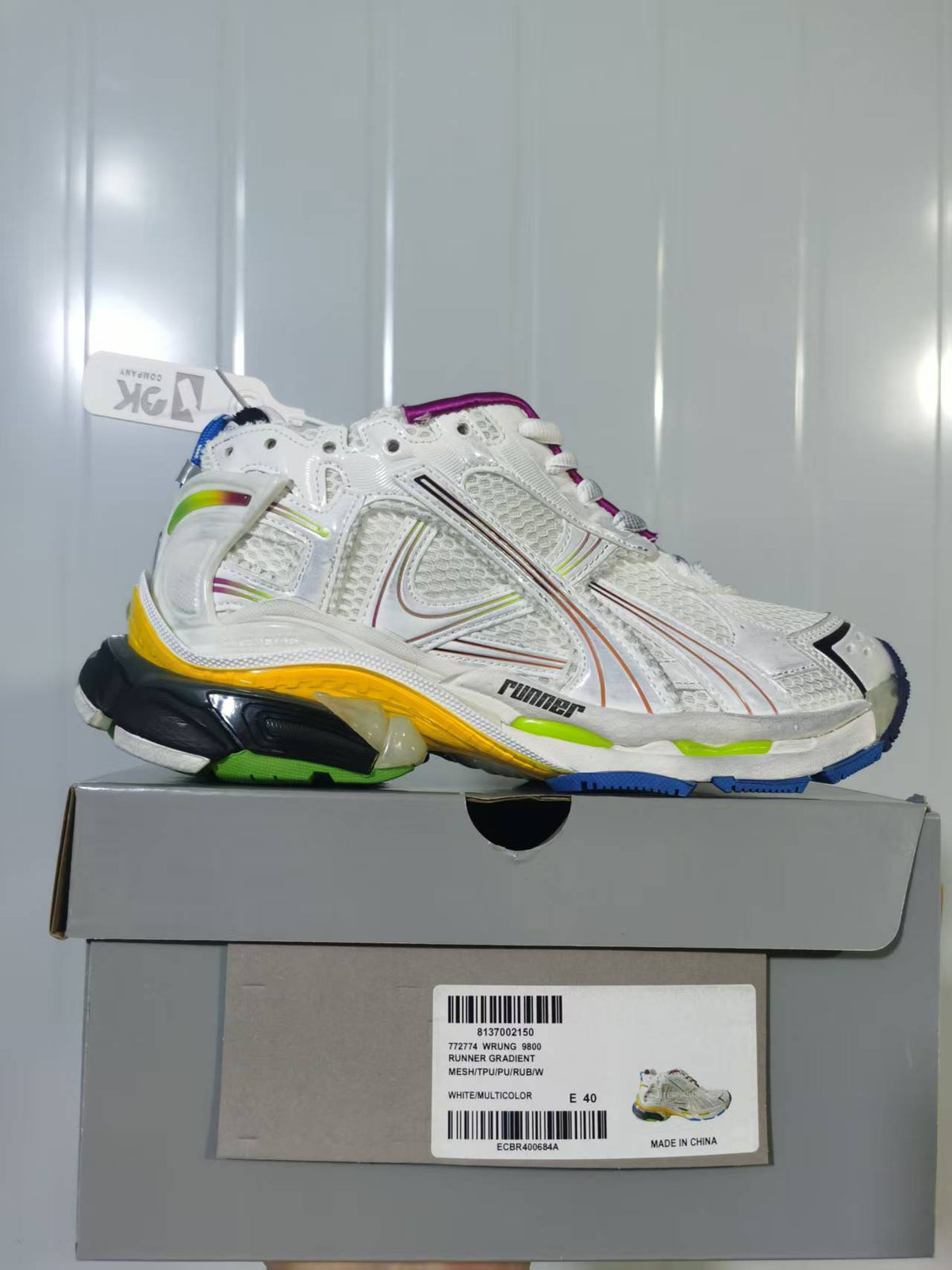 Side view of the white multicolor Puma Runner Gradient sneaker placed on its box, with the product label visible.