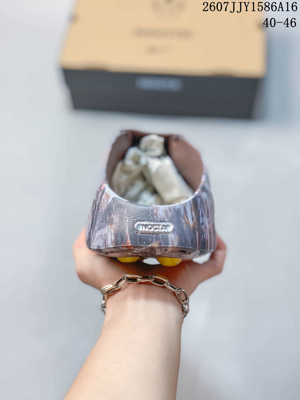 Rear view of a marbled sandal showing the heel branding detail and brown interior; the presentation box is in the background.