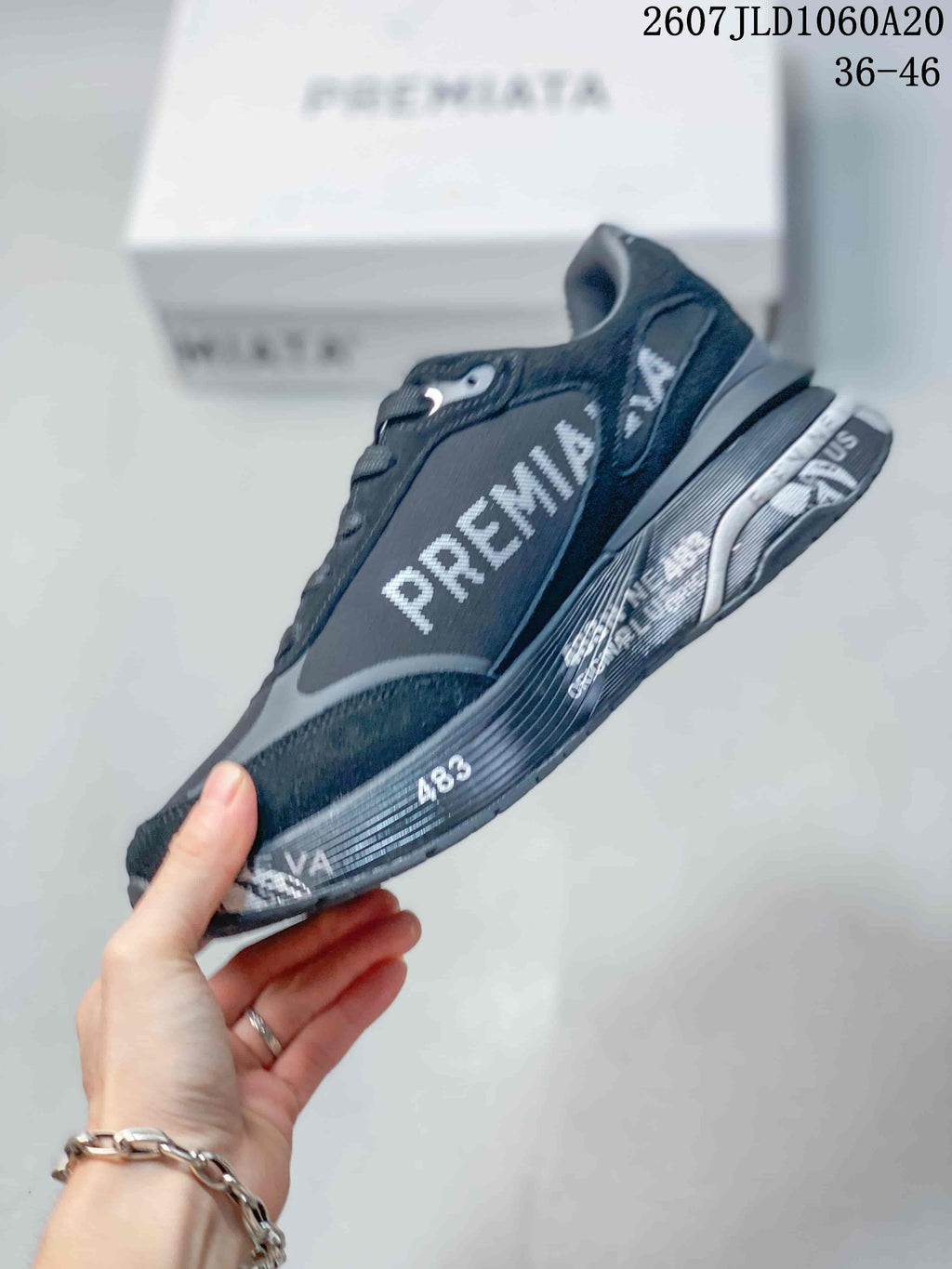 Side profile of a black and gray Premiata trainer showing the large side logo, layered panels, and printed midsole details.