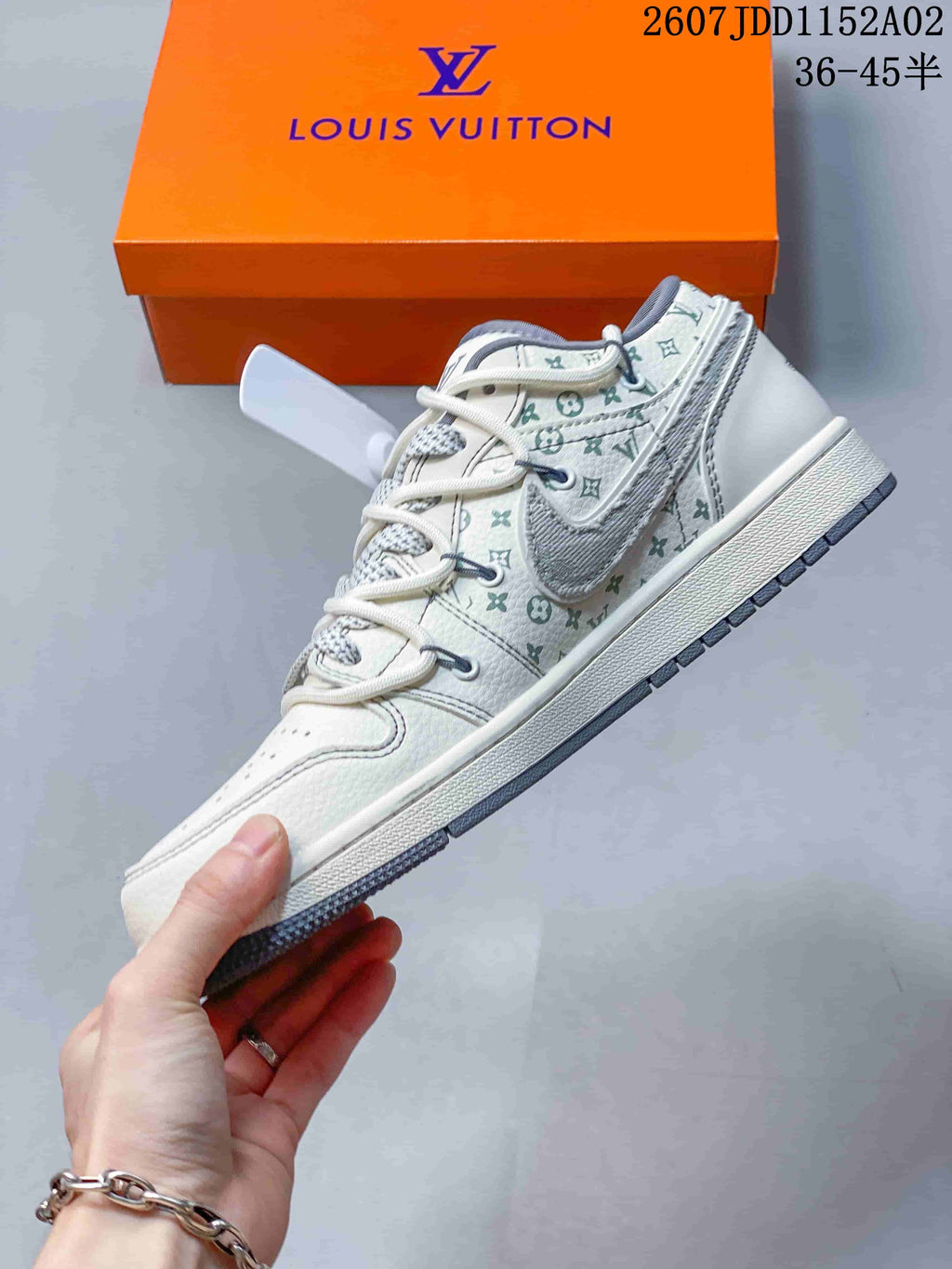 Side view of a white and gray low-top sneaker with monogram-style panels and a contrasting side emblem.