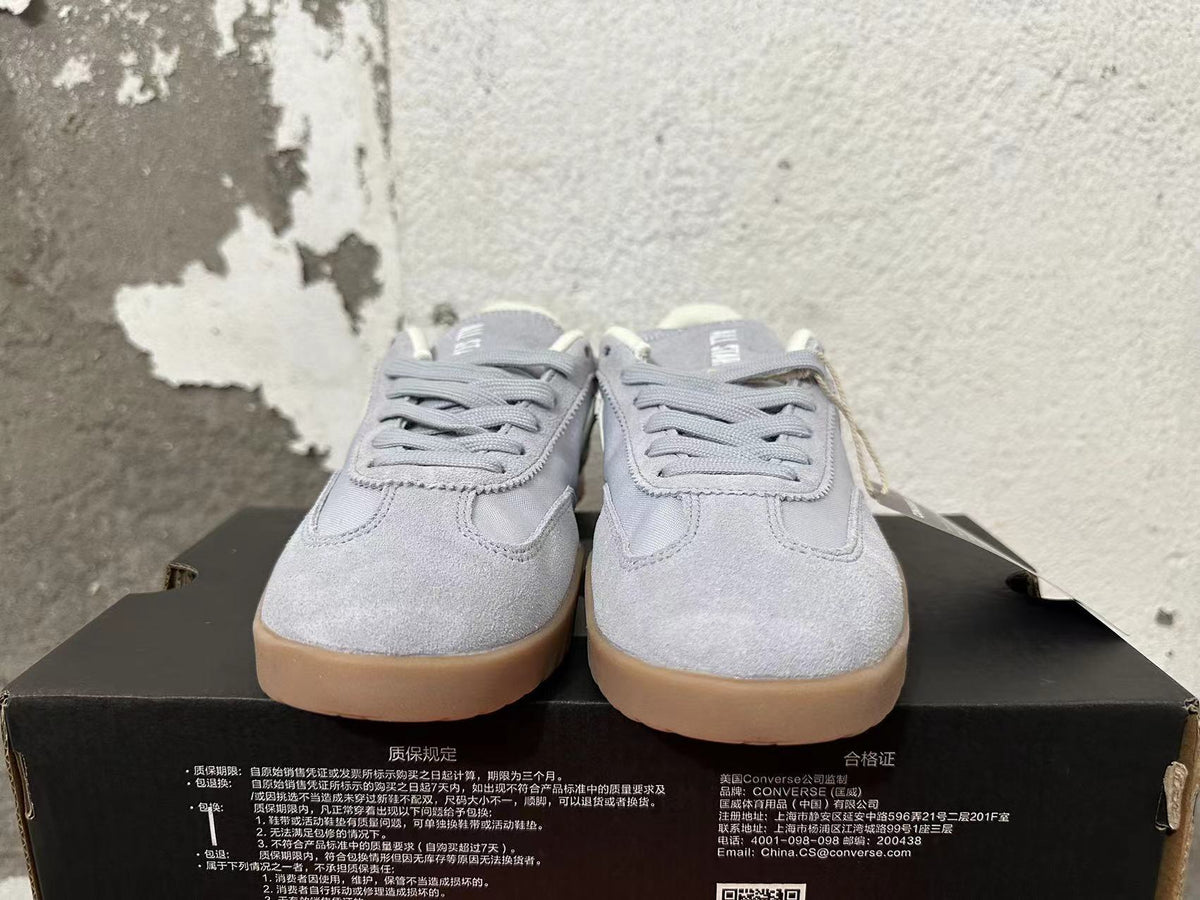 Front view of gray lace-up Converse trainer-style sneakers with gum-colored soles