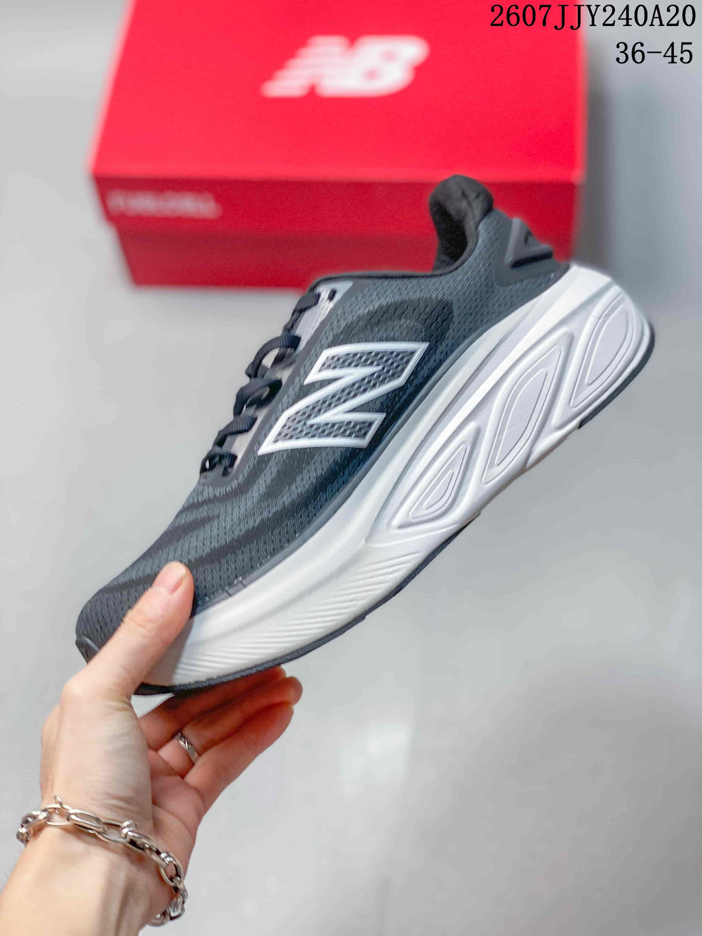 Side profile showing the dark gray textile-style upper, white New Balance logo, layered white midsole, and dark outsole.