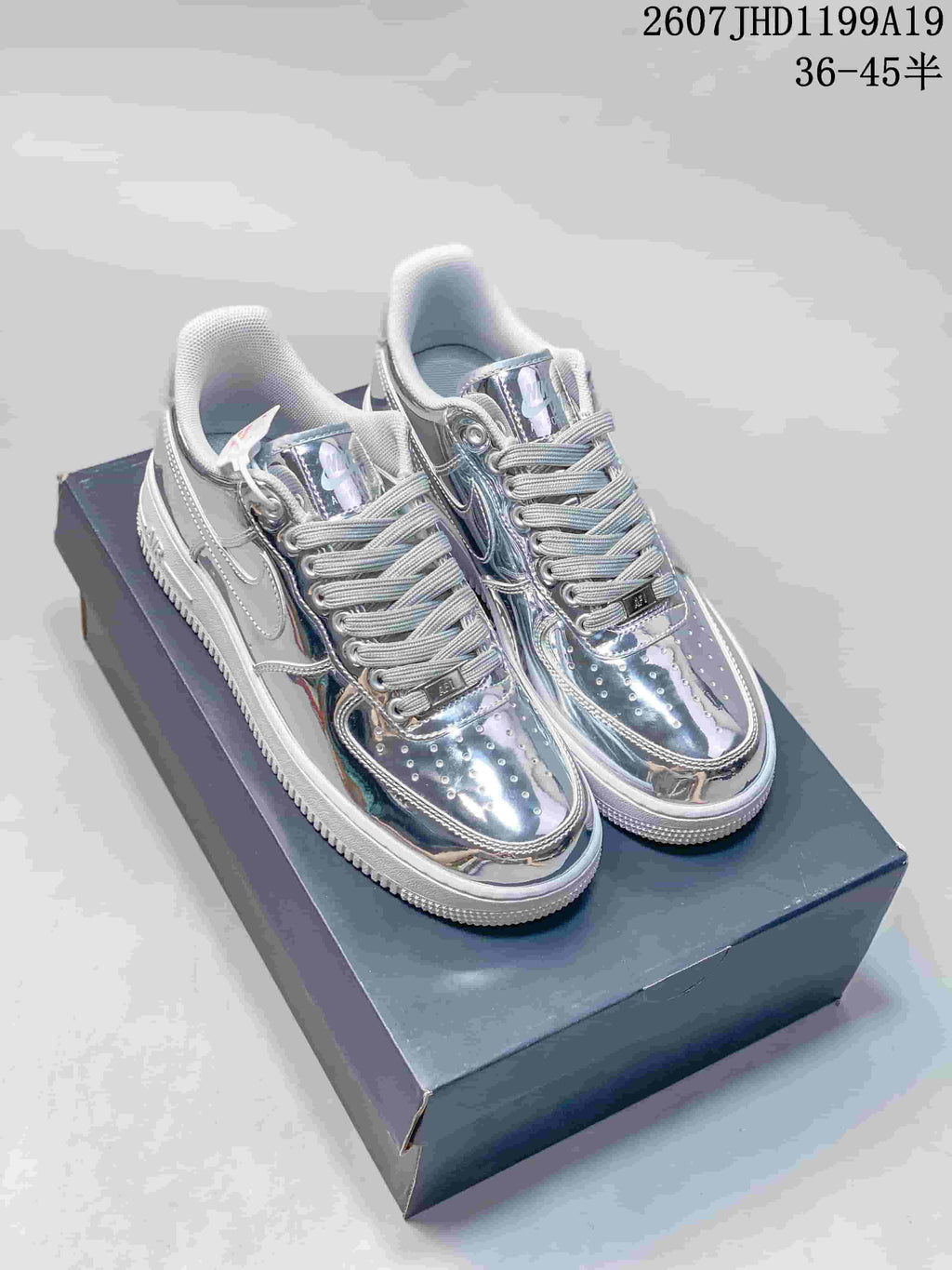 Pair of metallic silver Nike Air Force 1 low-top sneakers displayed on a shoe box; overlay text shows style code 2607JHD1199A19 and size range 36–45.