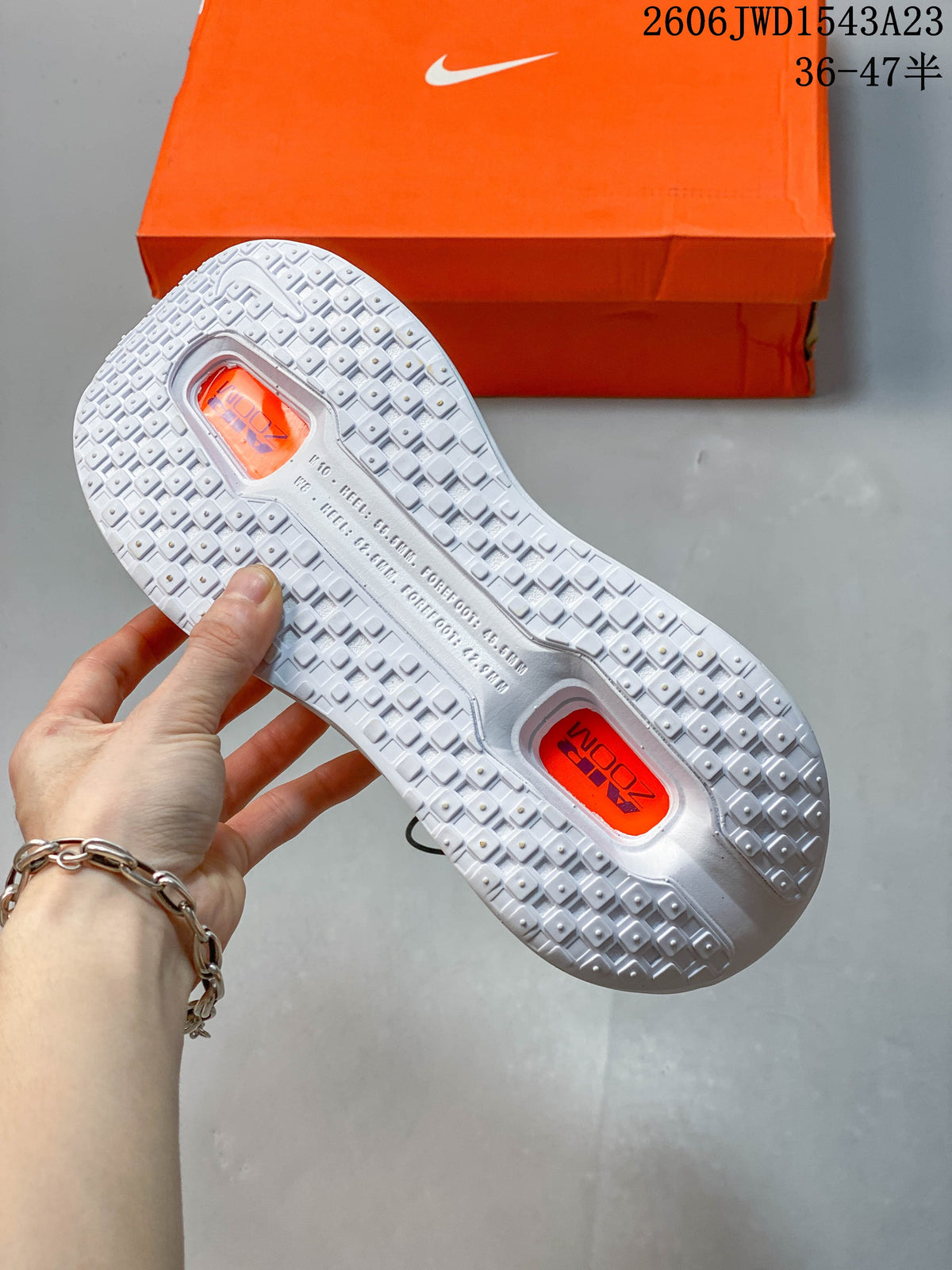 Close view of the white shoe outsole, showing its tread and orange-colored openings.