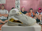 Side view of a light gray high-top sneaker with perforated panels and gold-tone accents