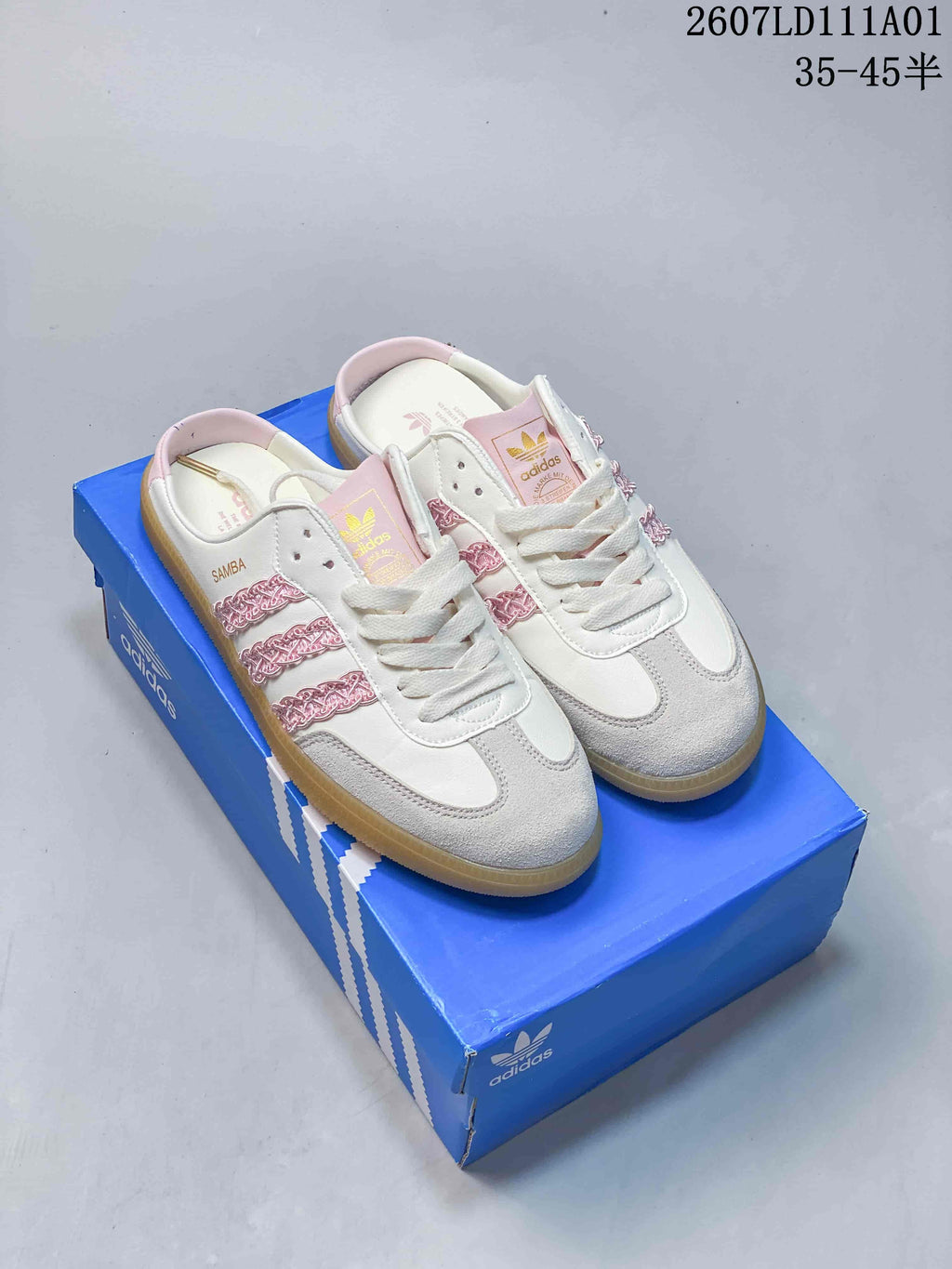 White and pink Adidas Samba OG Mule sneakers with grey toe overlays and a gum-colored outsole, shown on a blue box