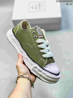 Angled side view of an olive MMY sneaker showing the canvas-like upper, white laces, tongue branding, and sculpted sole.